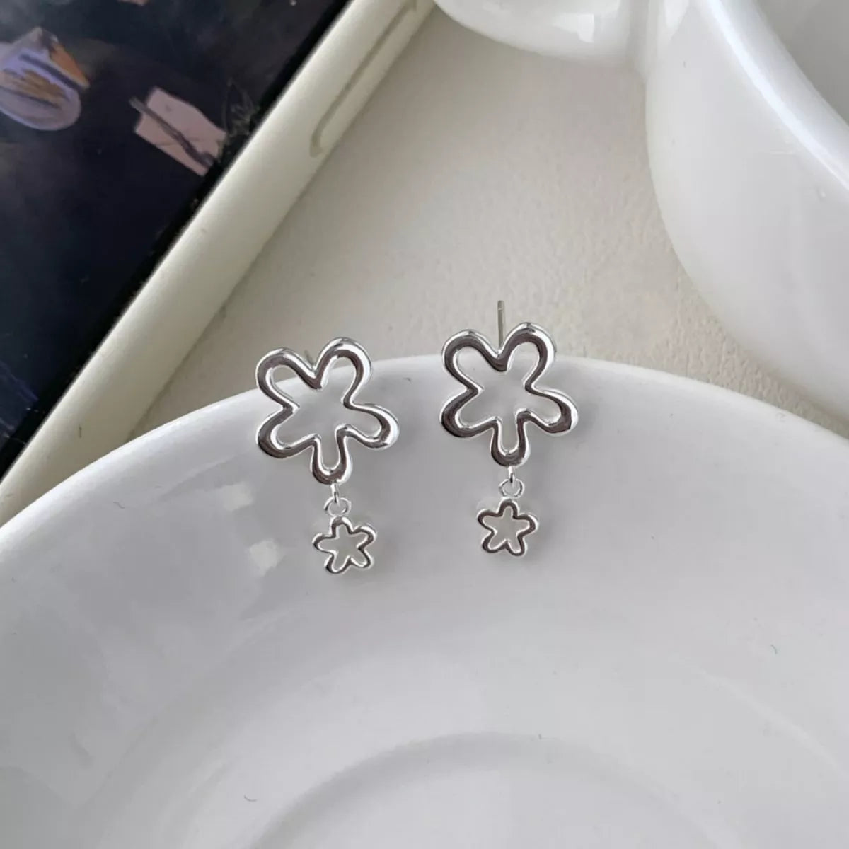 Pair of silver flower drop earrings displayed on a white dish