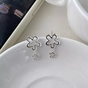 Pair of silver flower drop earrings displayed on a white dish