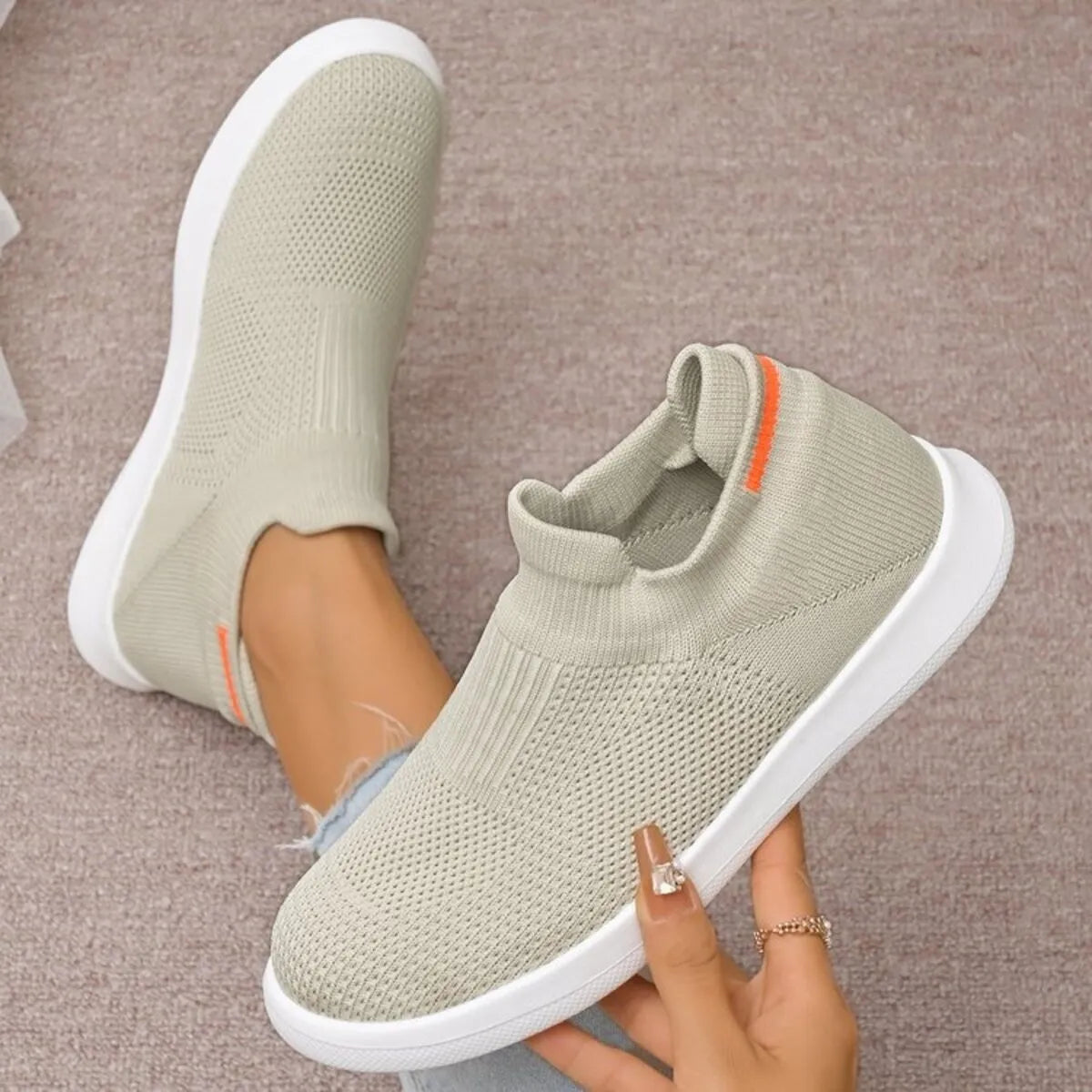 Beige knit slip-on shoe held beside the matching shoe worn on a foot