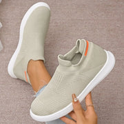 Beige knit slip-on shoe held beside the matching shoe worn on a foot