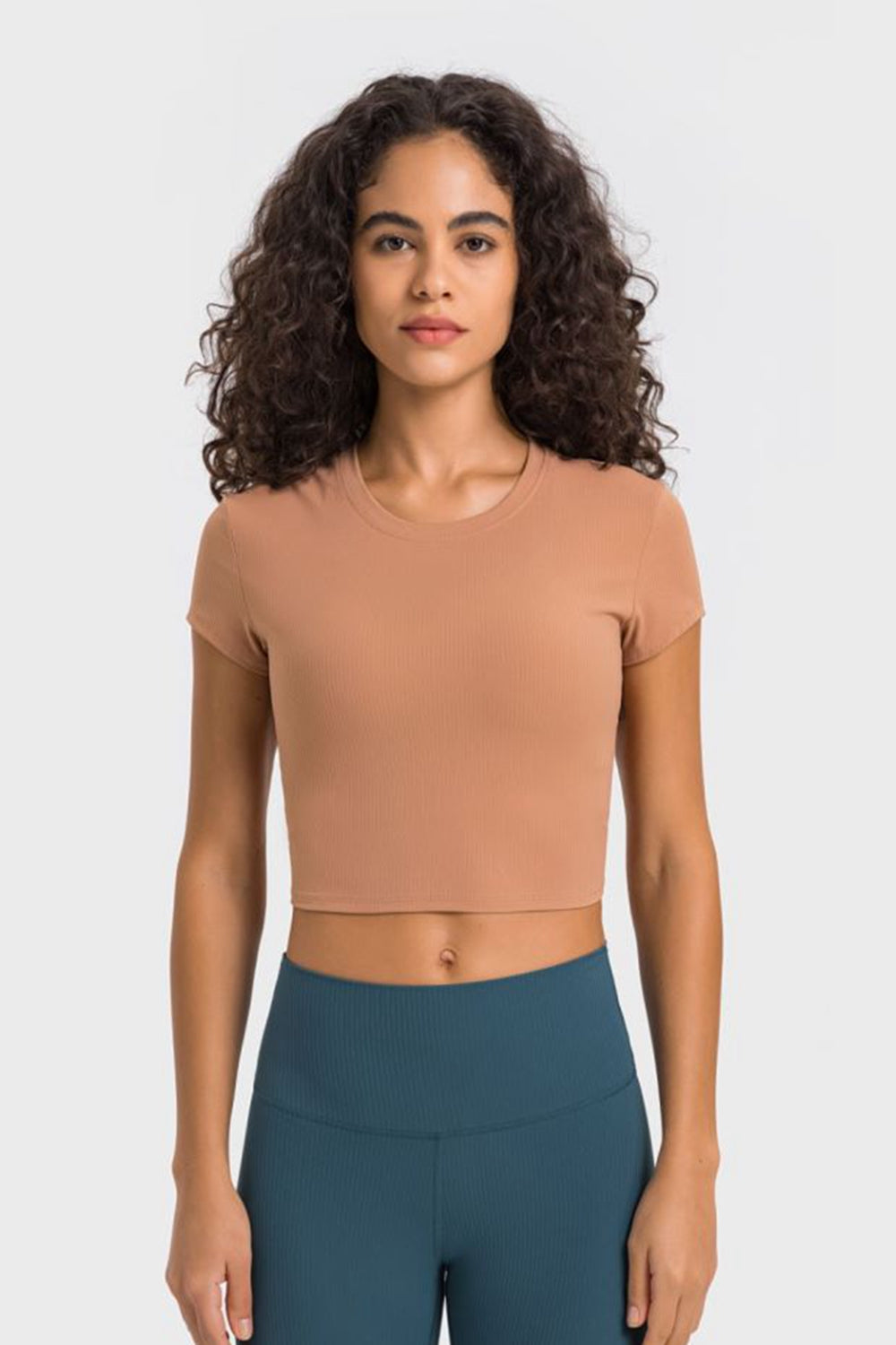 Model wearing a peach cropped T-shirt with teal leggings, front view