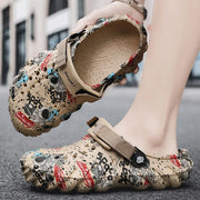 Beige graffiti-print clog held to show its textured footbed beside a matching shoe on a foot