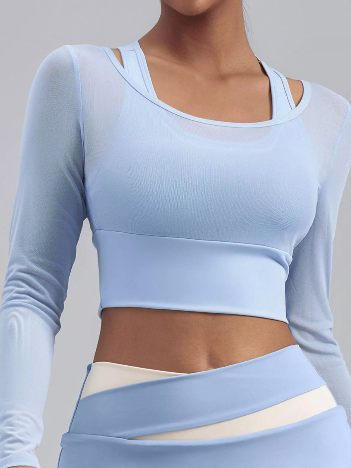 Close front view of light blue cropped active top with layered scoop neckline and matching waistband below