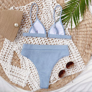 Light blue ribbed bikini set laid flat in a woven basket with sunglasses