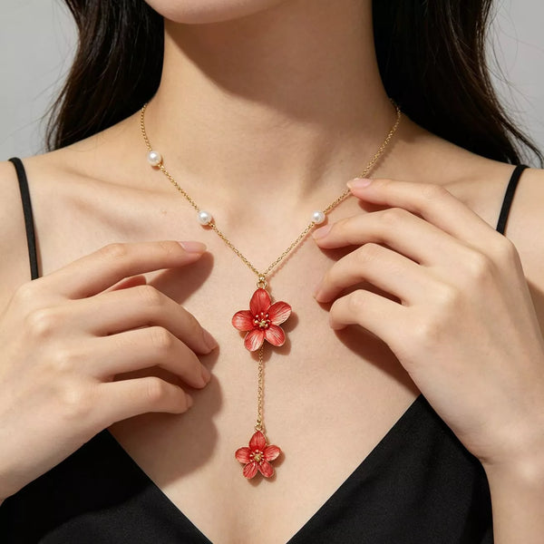 Gold-tone pearl necklace with two red flower pendants worn over a black top