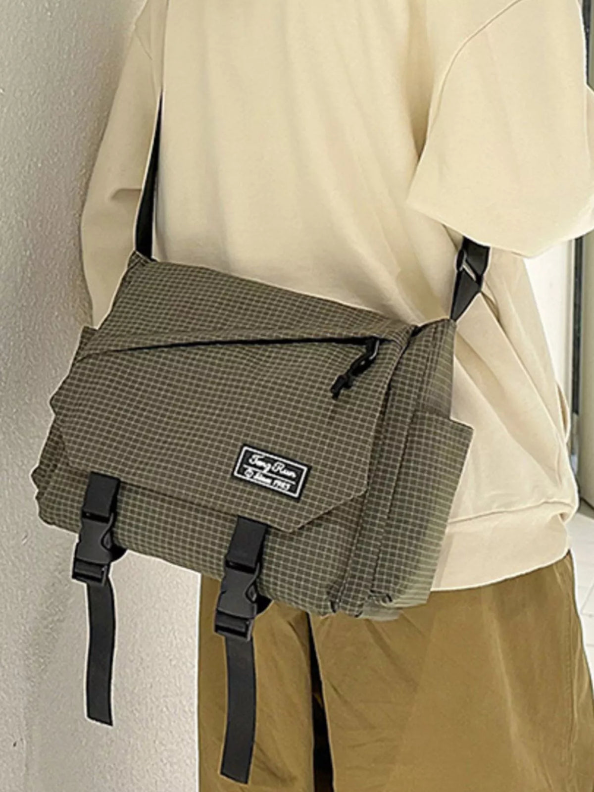 Olive checked crossbody bag showing flap front and adjustable black strap, worn at the hip