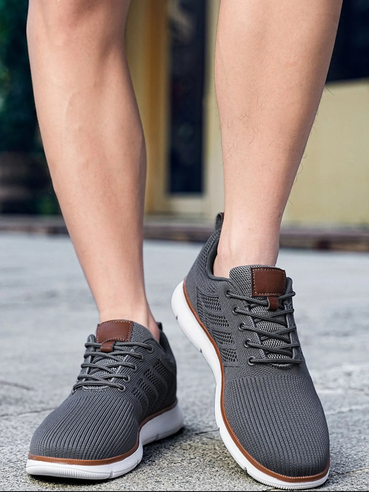 Front view of grey knit lace-up shoes with white soles, worn outdoors
