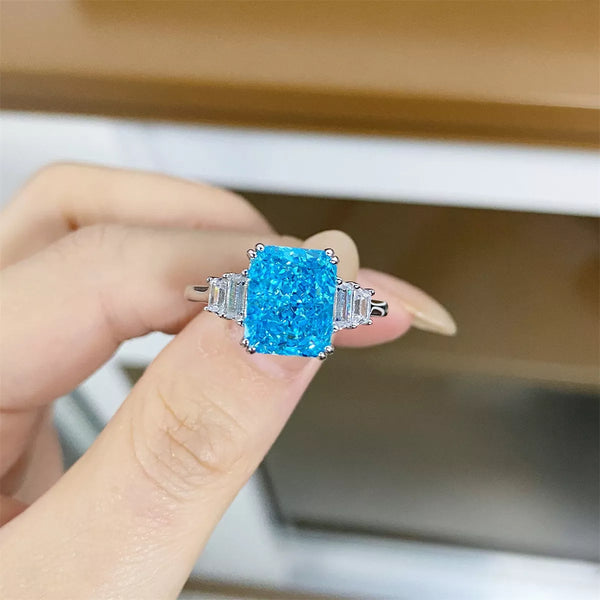 Pastel blue zircon ring held between fingers, showing rectangular center stone and baguette sides