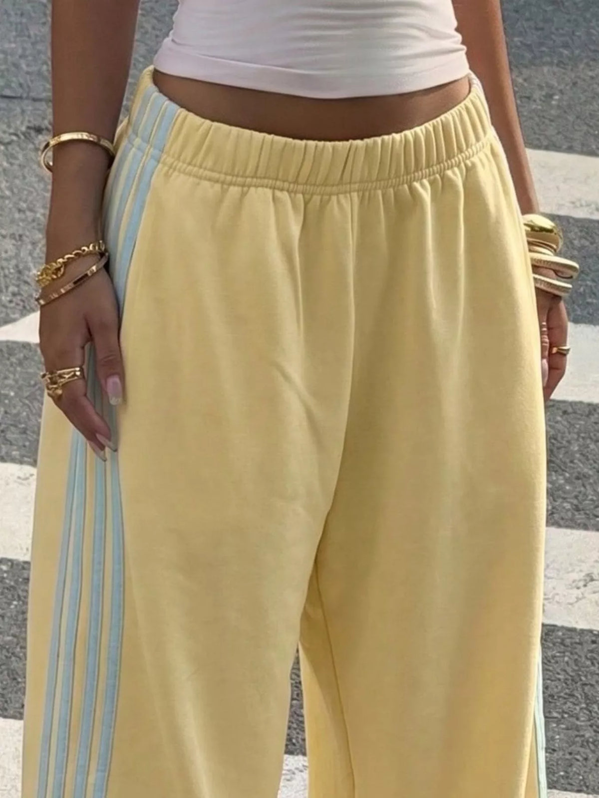 Yellow wide-leg track pants with white side stripes, front view