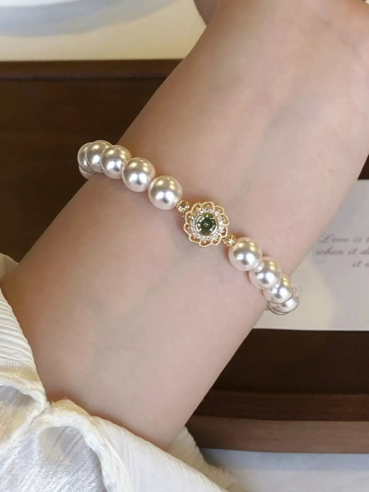 Pearl flower bracelet worn on the wrist, showing its green-centered gold charm