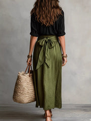 Rear view of black shirt paired with olive green midi skirt tied at the waist.