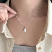 Model holding a silver feather pendant necklace against a cream shirt