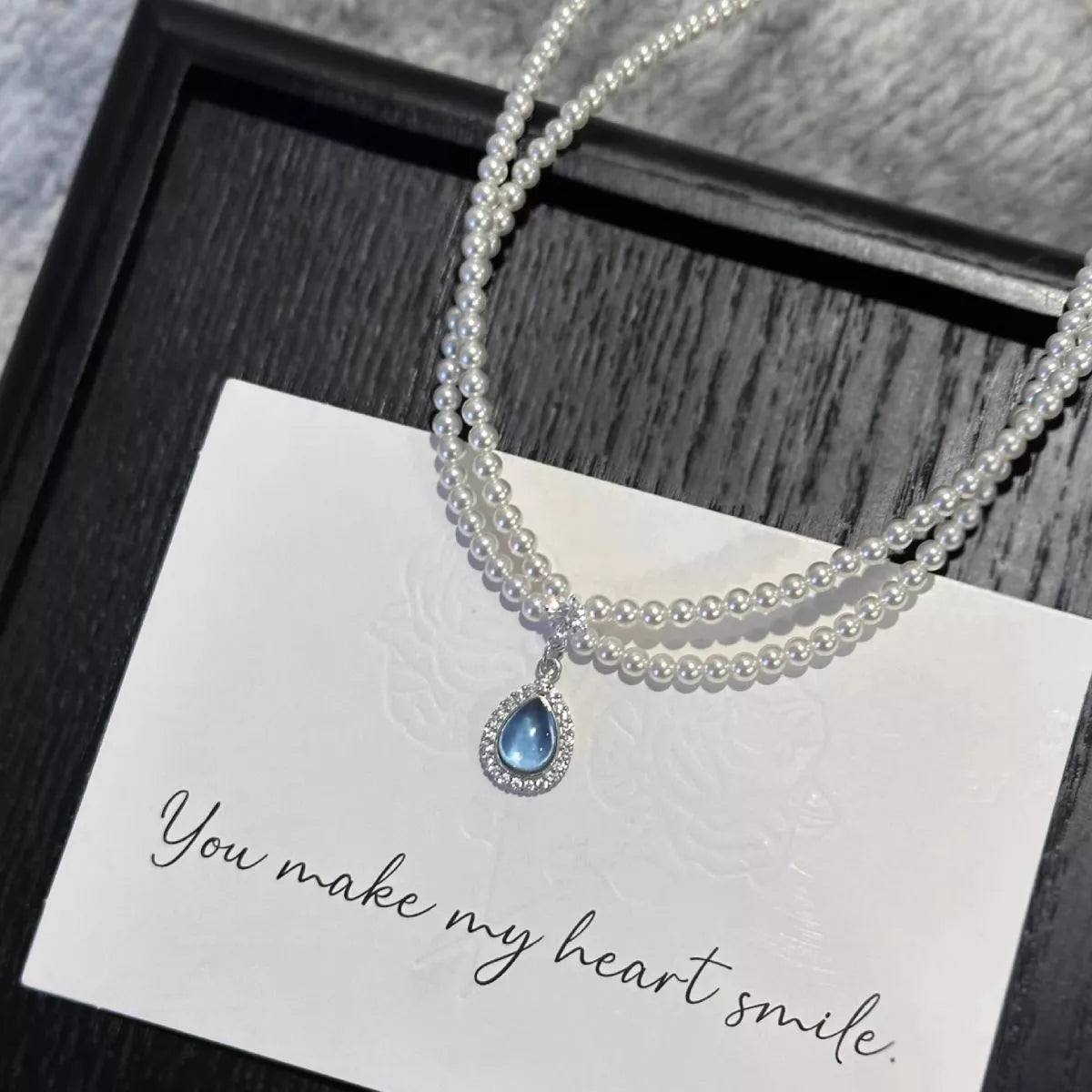 Double-layer pearl necklace with blue teardrop pendant on a card