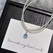 Double-layer pearl necklace with blue teardrop pendant on a card