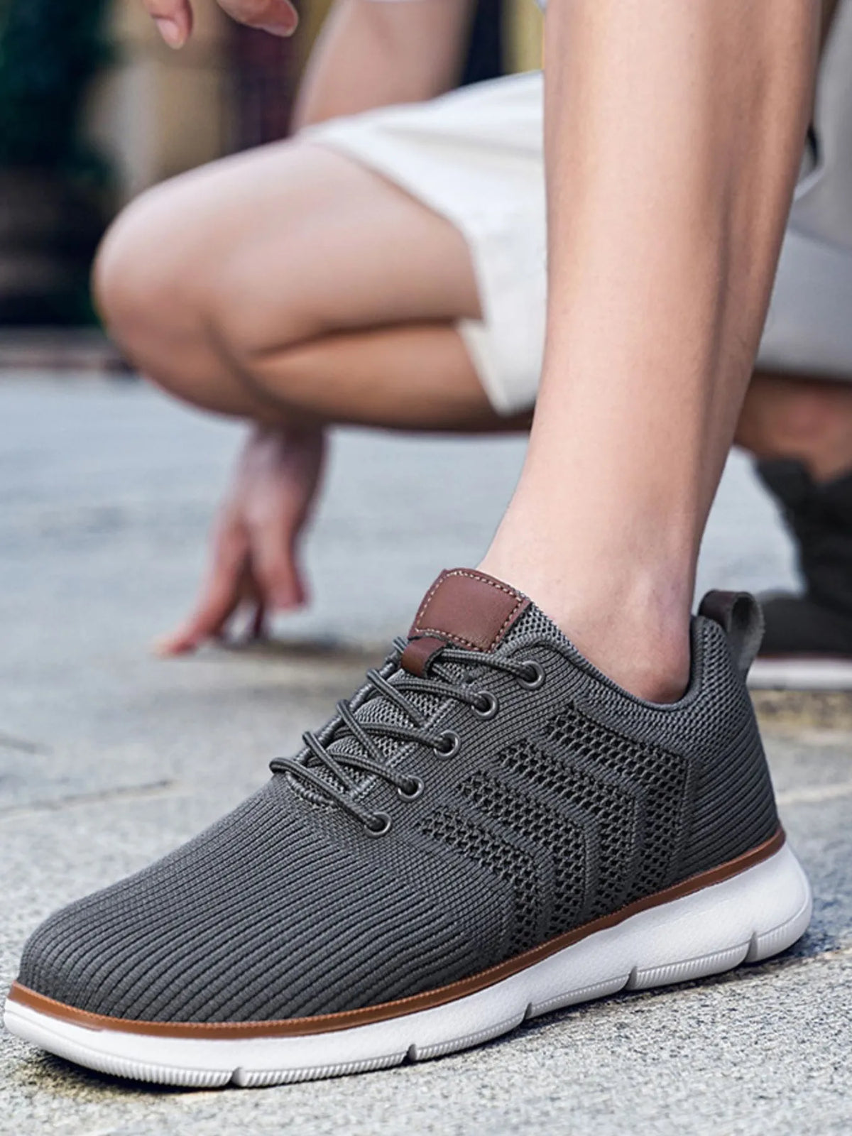 Close side view of a dark grey knit lace-up shoe with white sole and brown tongue patch