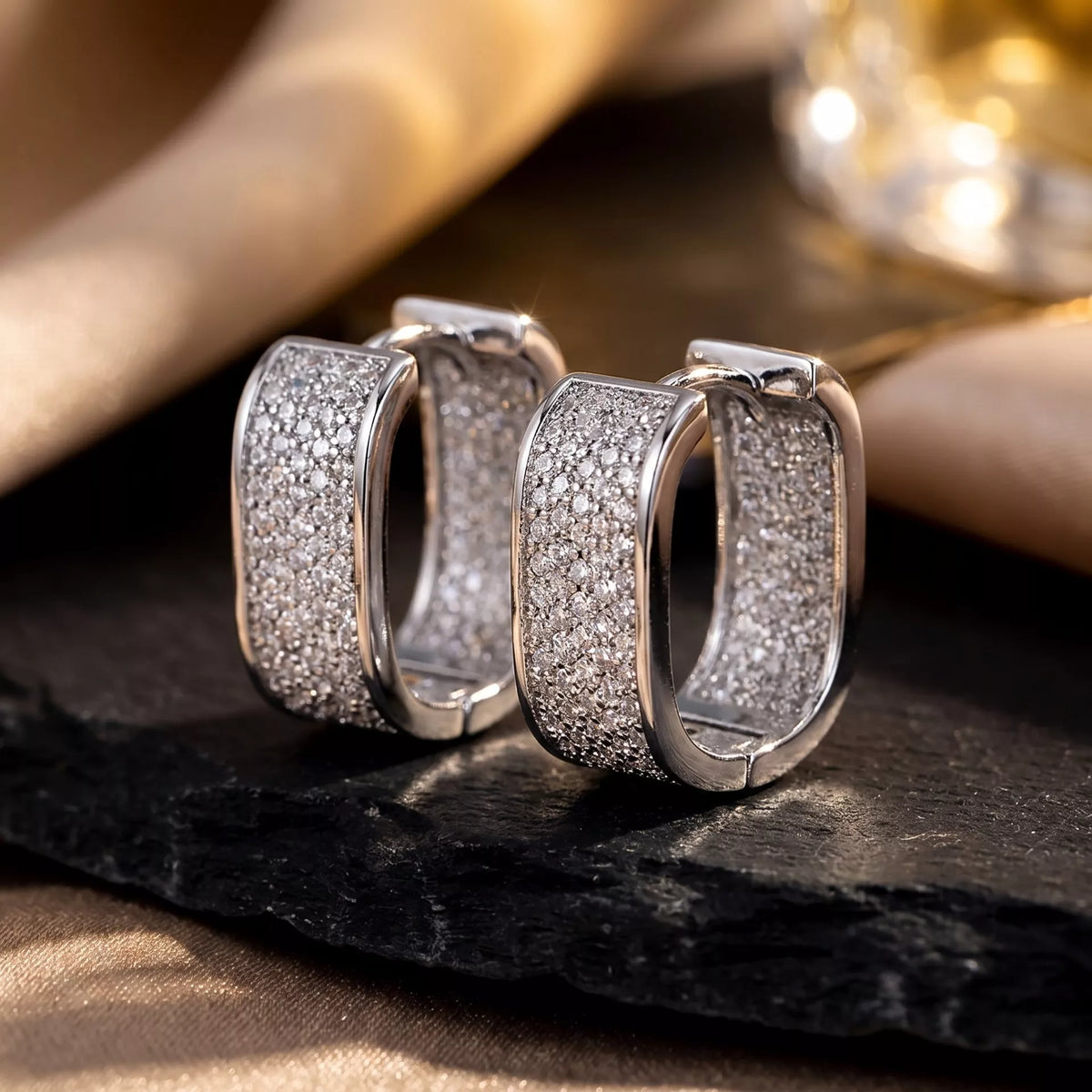Silver-tone square hoop earrings with clear stones on dark fabric