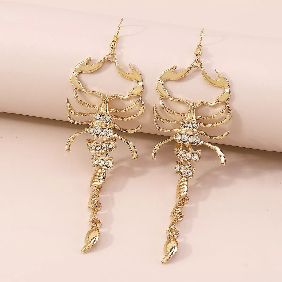 Pair of gold-tone scorpion dangle earrings with clear accents on a wrist