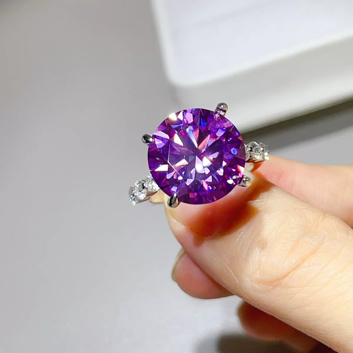 Close-up of purple round moissanite ring held between fingers