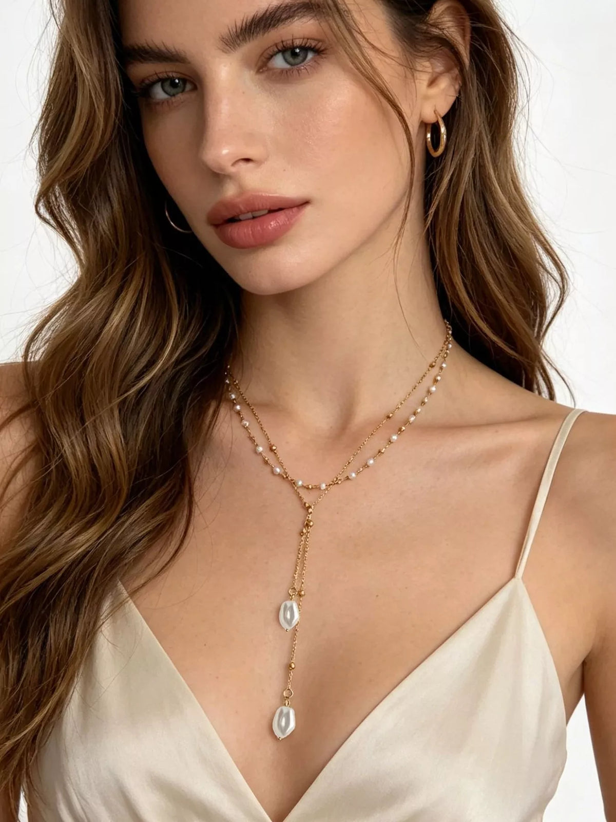 Gold-tone pearl Y necklace with two white pendants worn over a light top