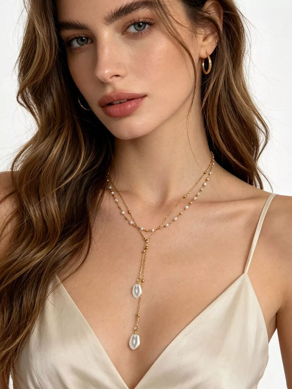 Gold-tone pearl Y necklace with two white pendants worn over a light top