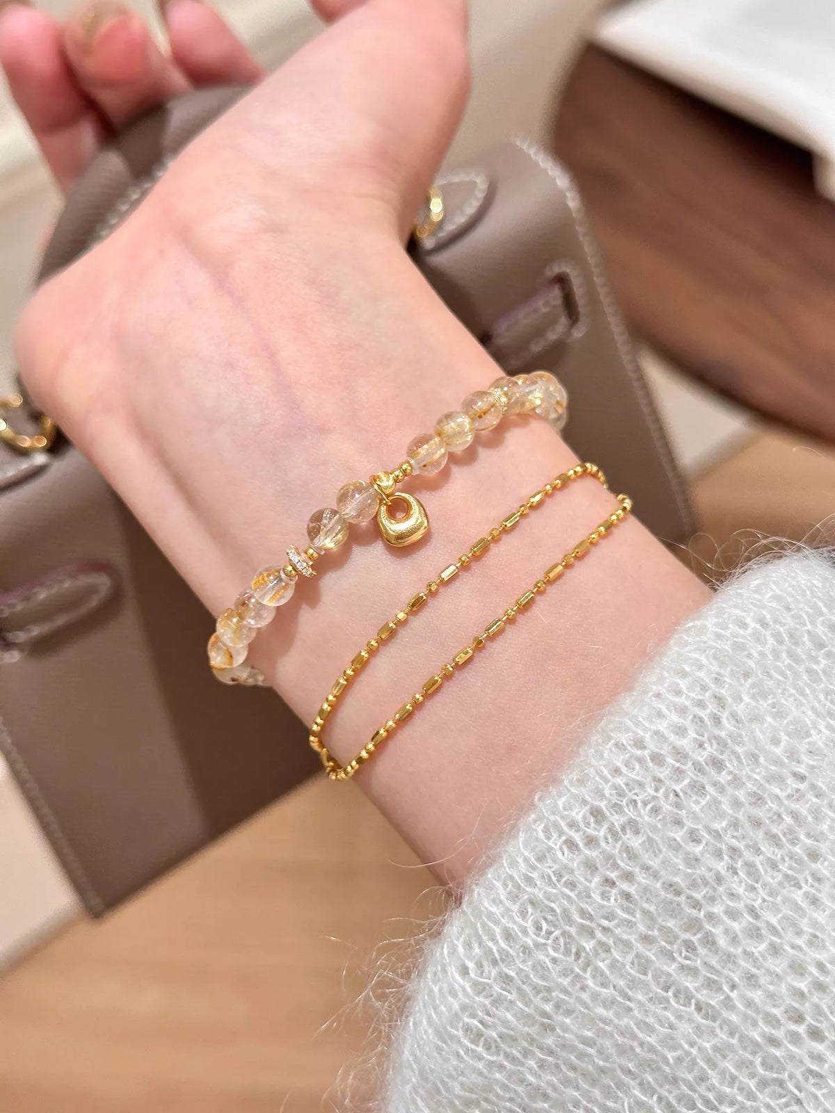 Two slim gold-tone bracelets worn together on a wrist, including a beaded charm strand.