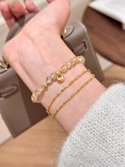 Two slim gold-tone bracelets worn together on a wrist, including a beaded charm strand.