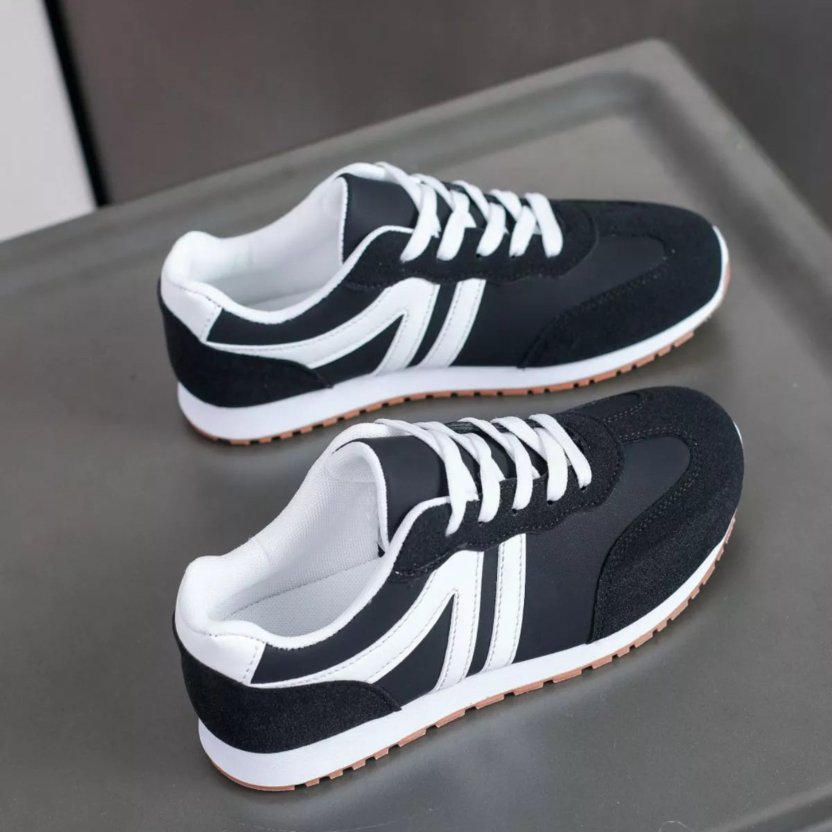 Pair of black lace-up sneakers with white stripes, angled view