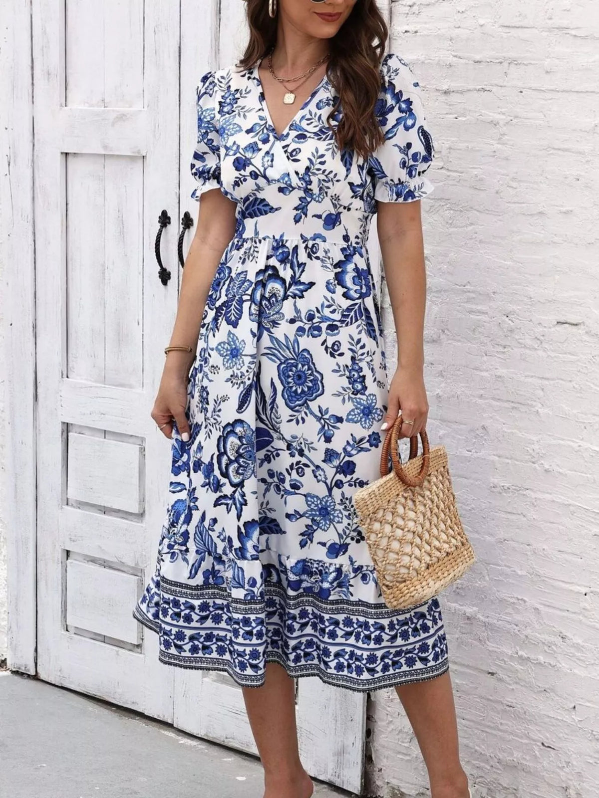 Blue and white floral puff-sleeve midi dress shown standing with a woven bag.