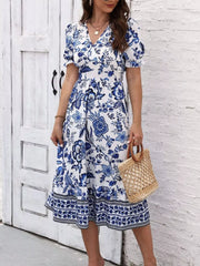 Blue and white floral puff-sleeve midi dress shown standing with a woven bag.