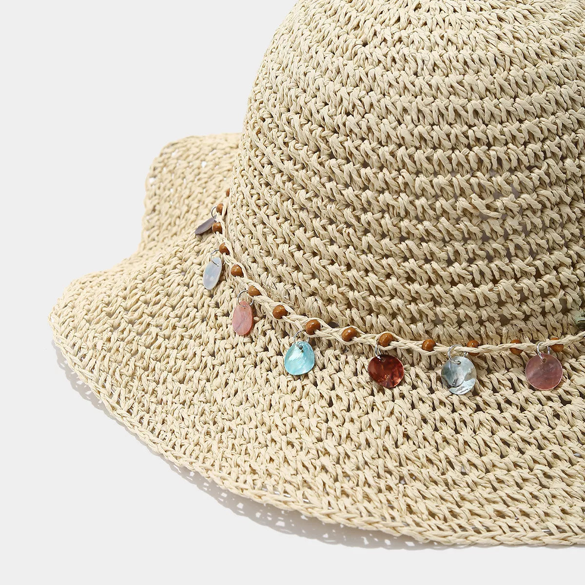 Close-up of the multicolour disc trim on the beige straw-woven hat