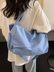 Blue travel bag carried over one shoulder, showing its long strap and front pocket