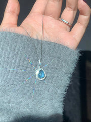 Blue teardrop pendant and fine chain laid across a hand