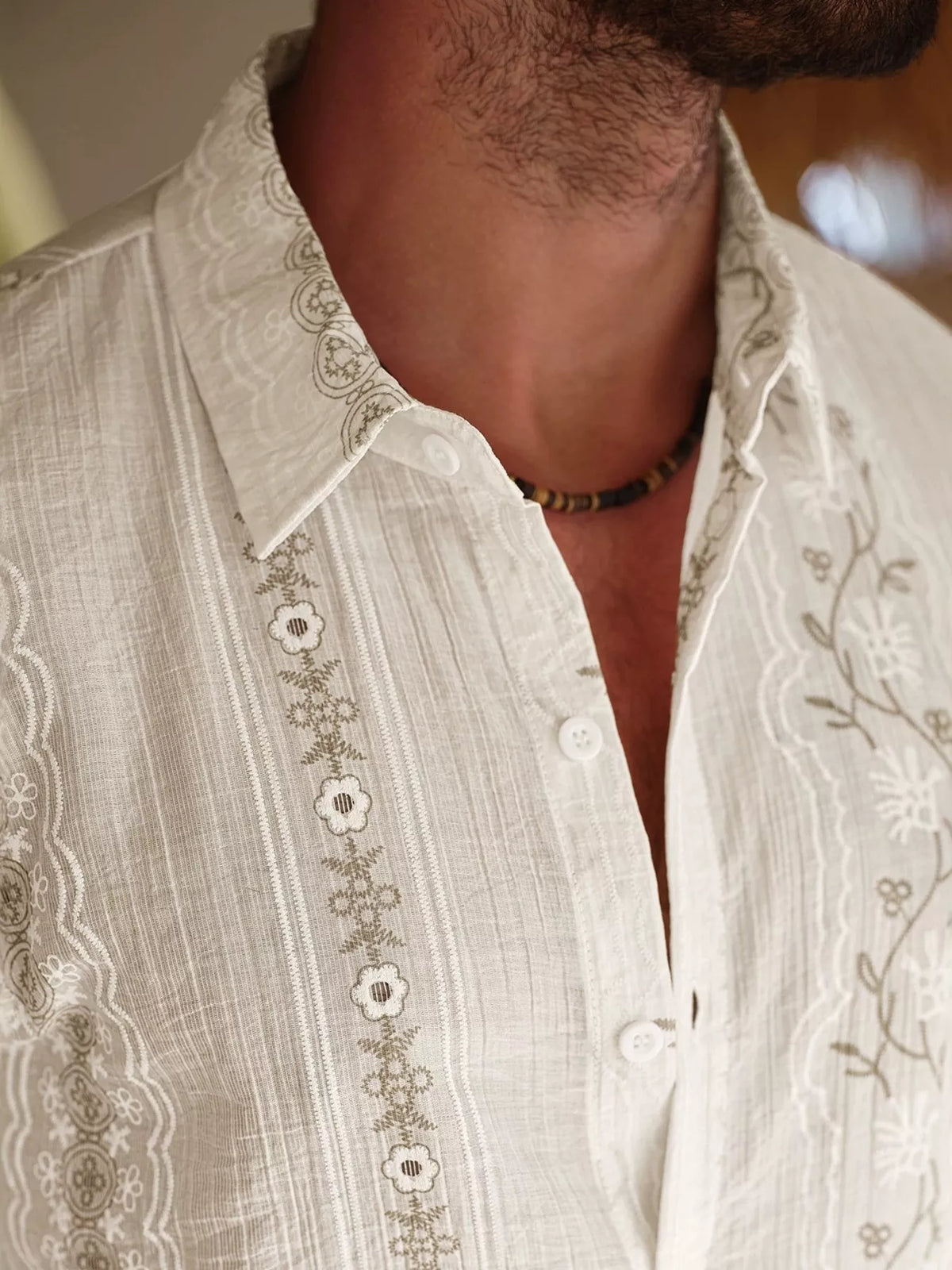 Close-up of flower-shaped buttons and embroidered vertical trim on cream shirt