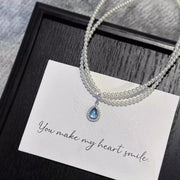 Pearl necklace with blue teardrop pendant on a message card