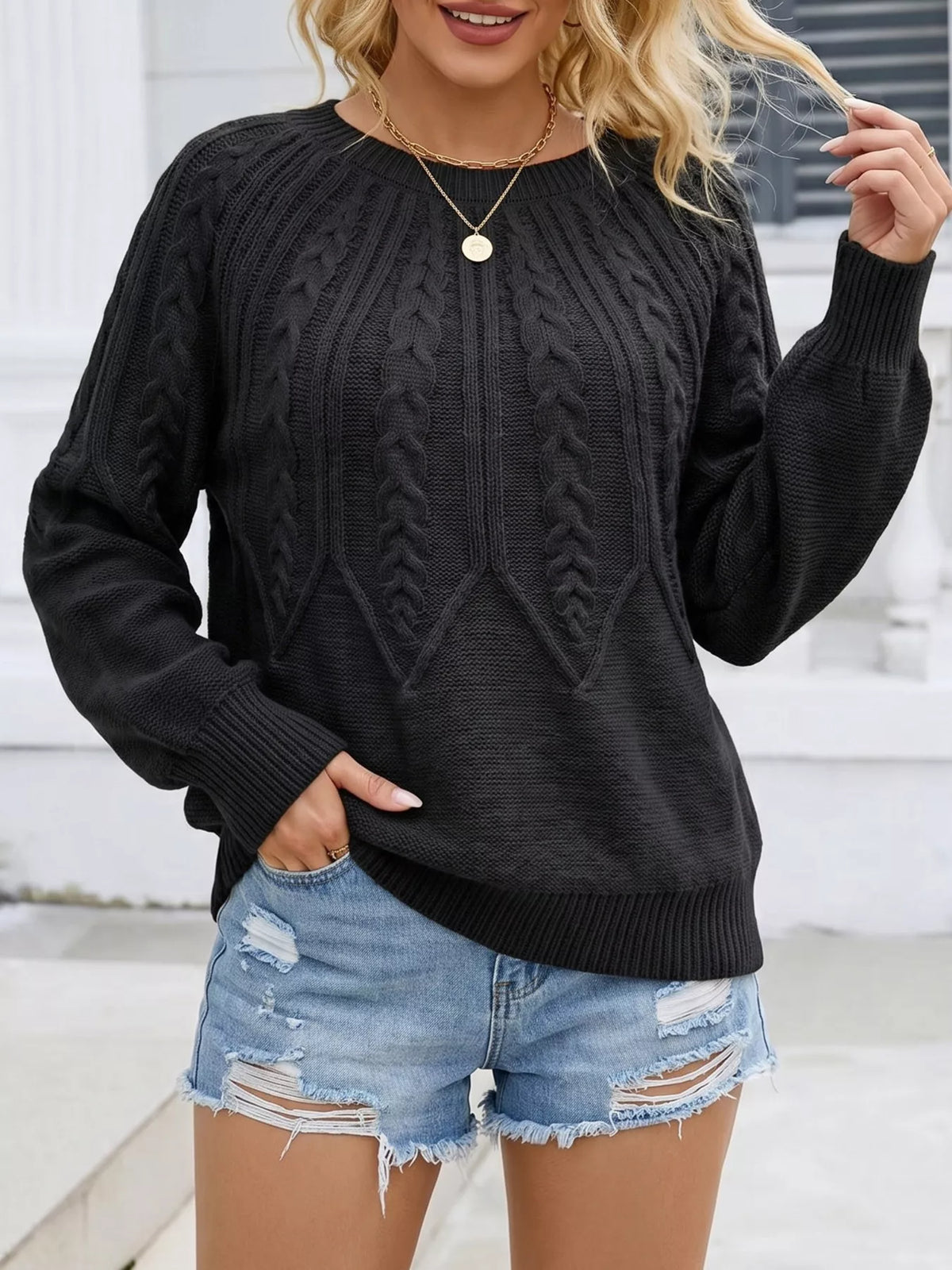 Front view of a black cable-knit sweater with distressed denim shorts