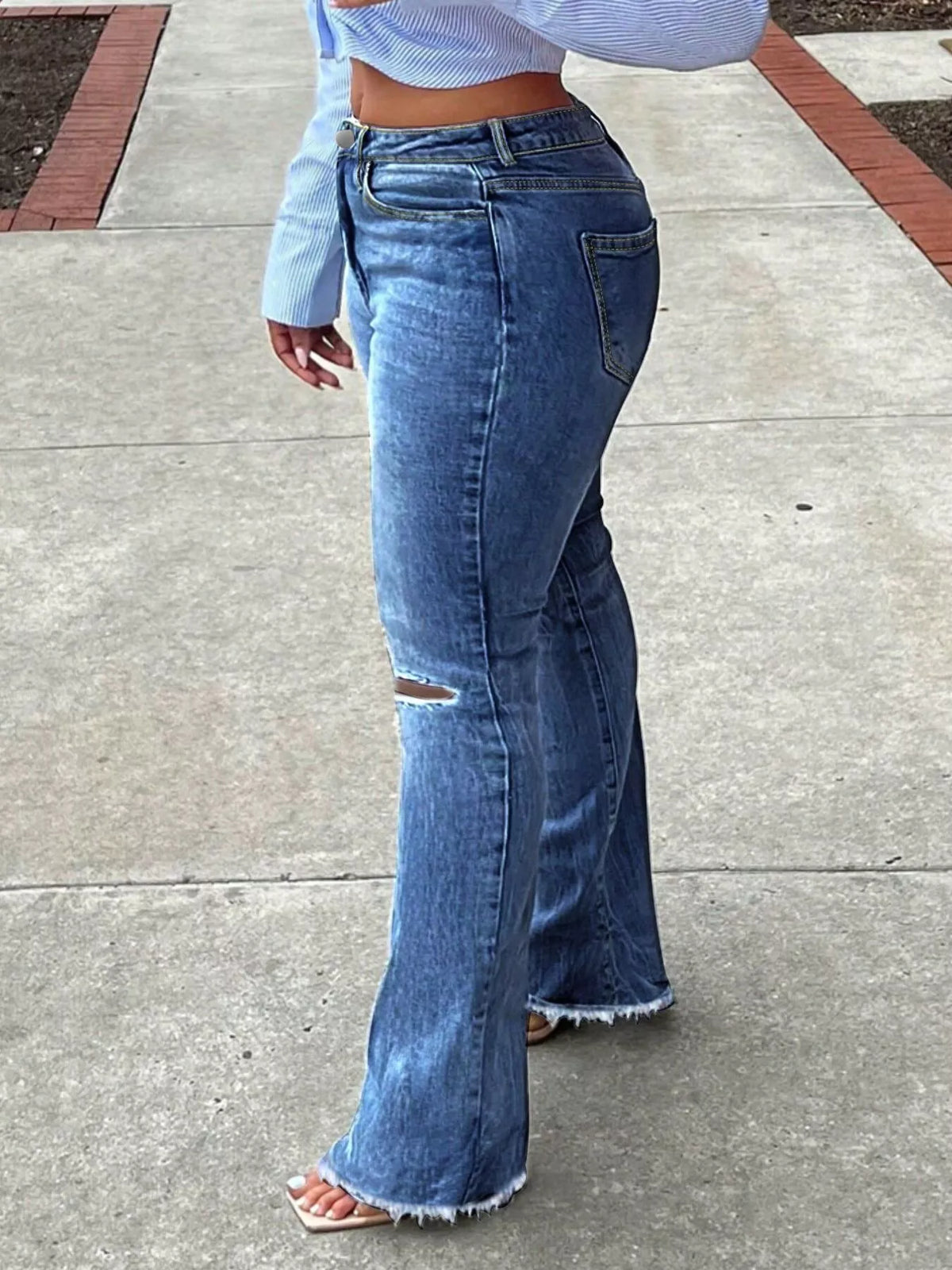 Side view of dark blue ripped-knee flare jeans with a high waist and flared hem.
