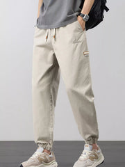 Angled front view of light beige men's joggers with elastic cuffs and side pockets.