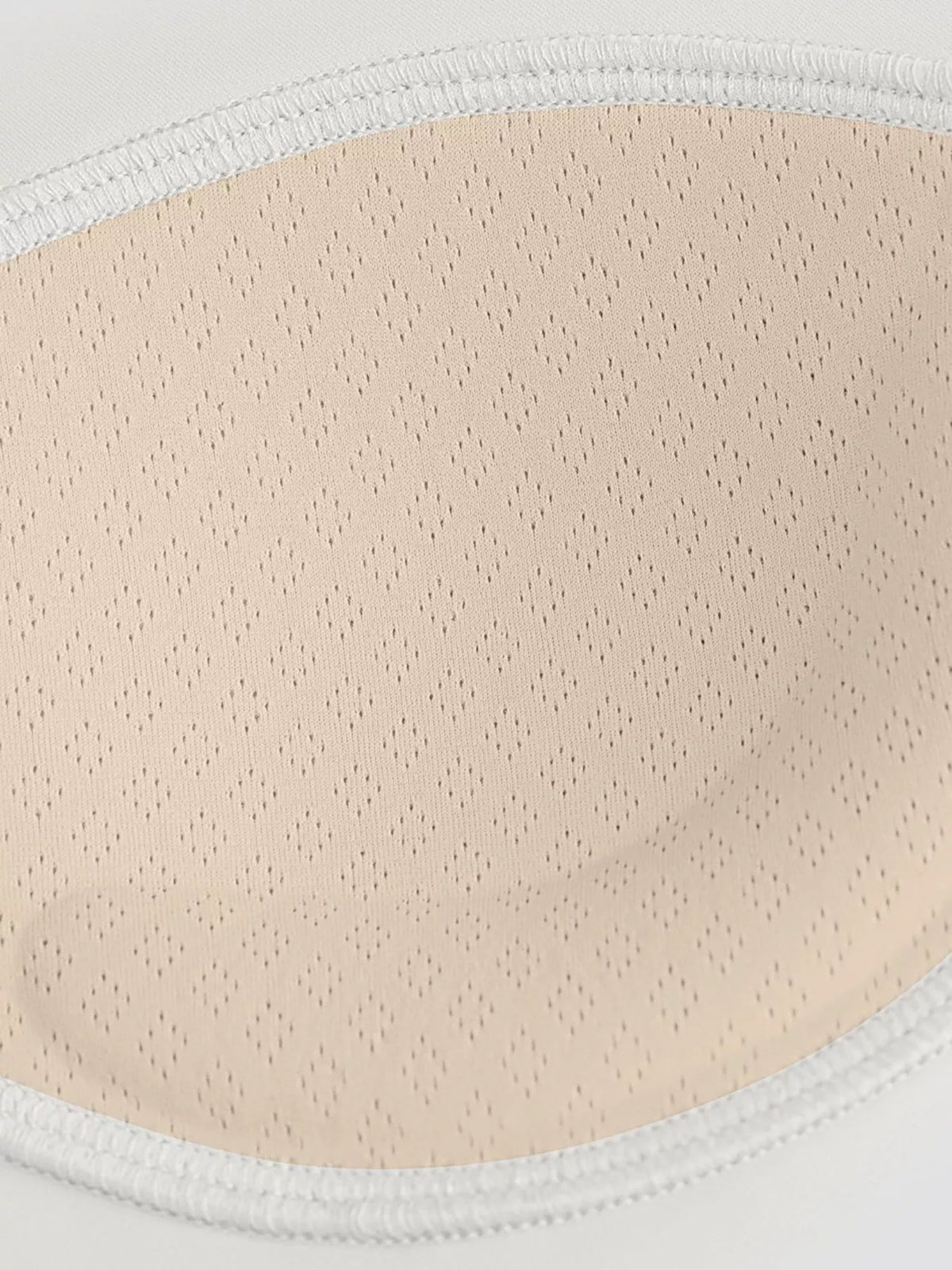 Close-up of perforated beige bra padding inside a white stitched fabric edge