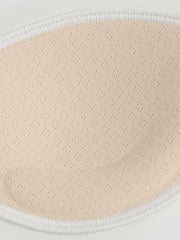 Close-up of perforated beige bra padding inside a white stitched fabric edge