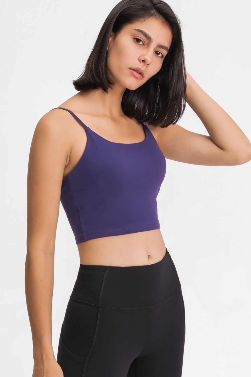 Model wearing a purple scoop-neck cropped cami with black leggings, turned slightly sideways.