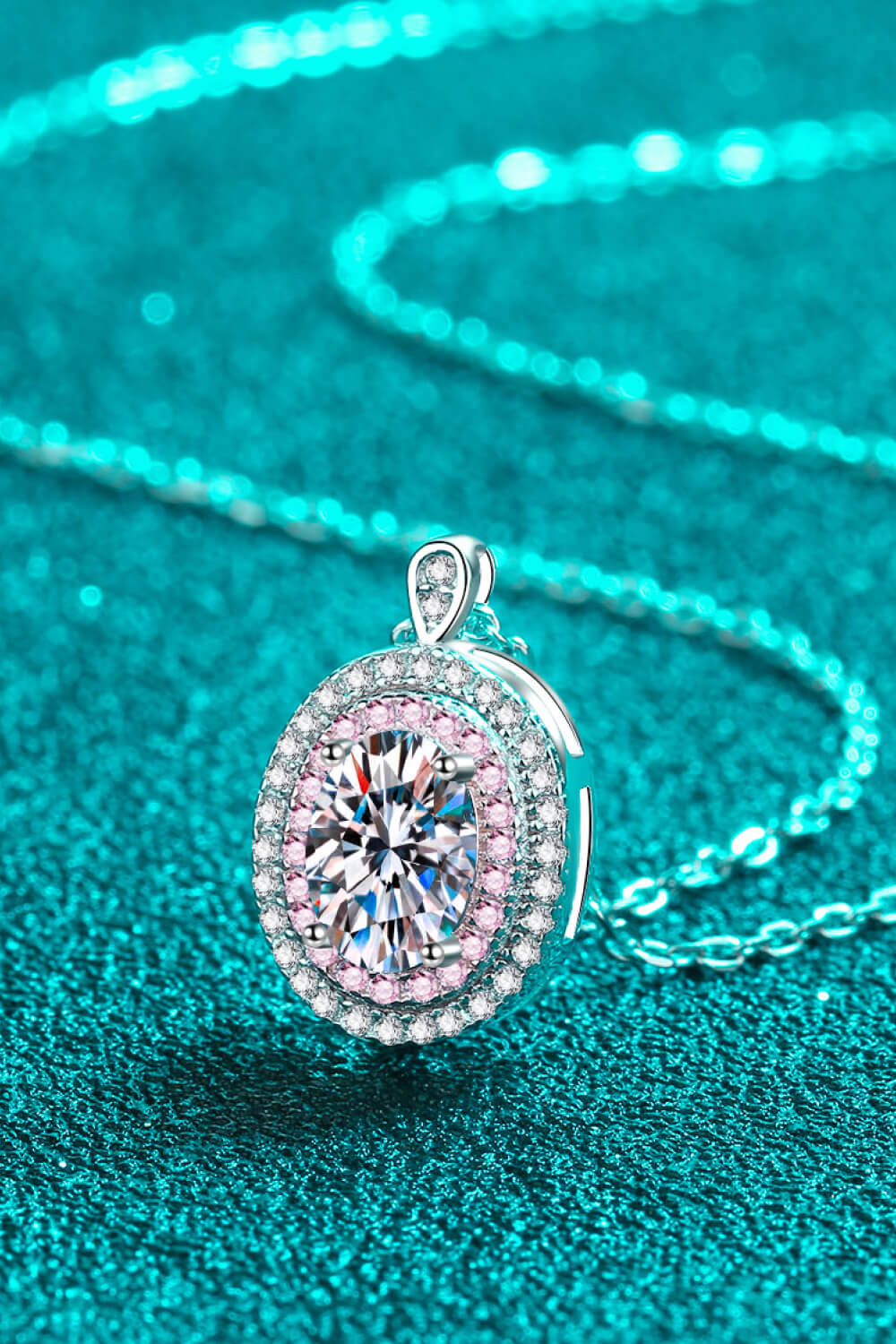 Angled close-up of an oval pink-bordered pendant and chain on teal