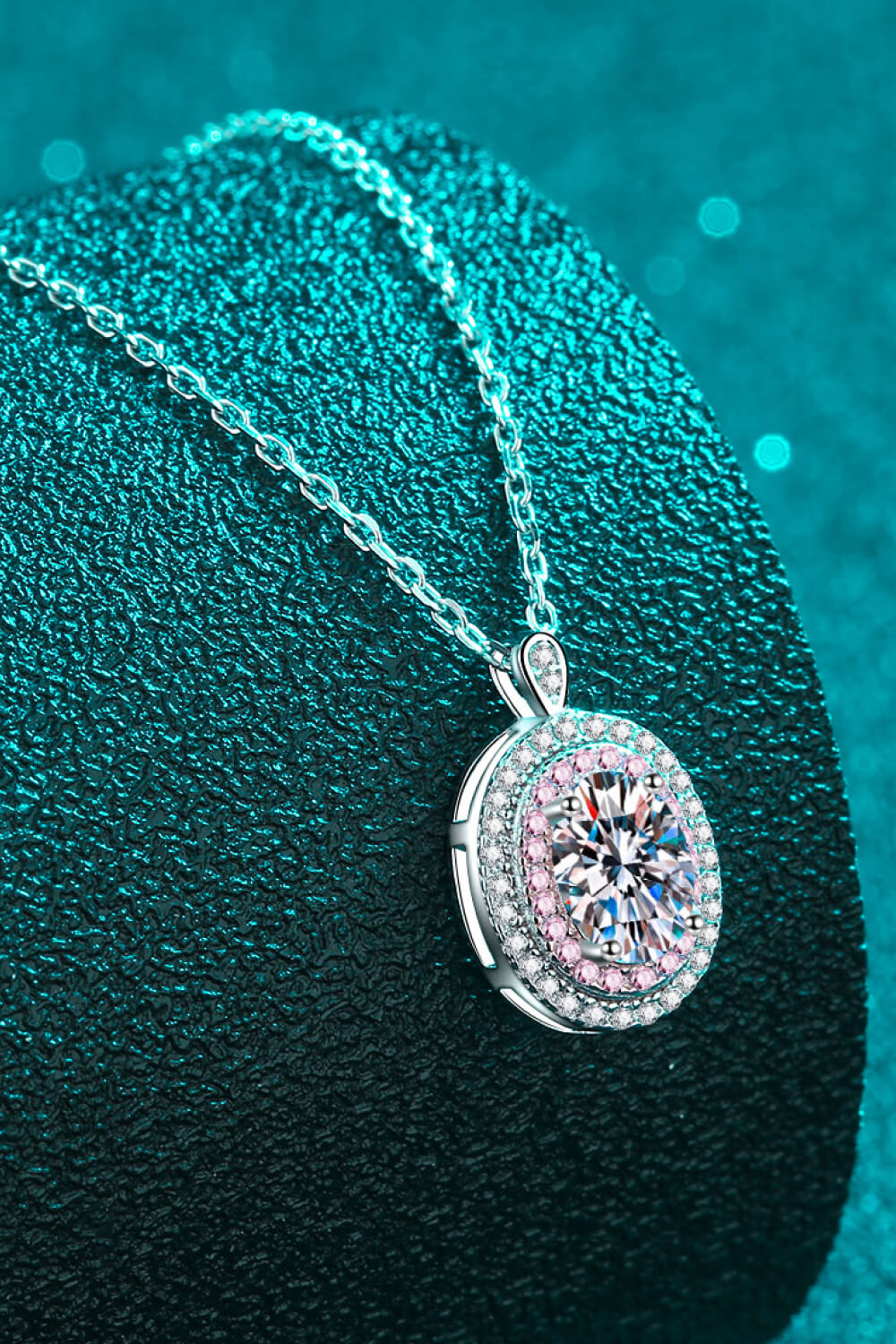 Oval pink-bordered pendant necklace draped over a teal cushion