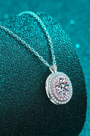 Oval pink-bordered pendant necklace draped over a teal cushion