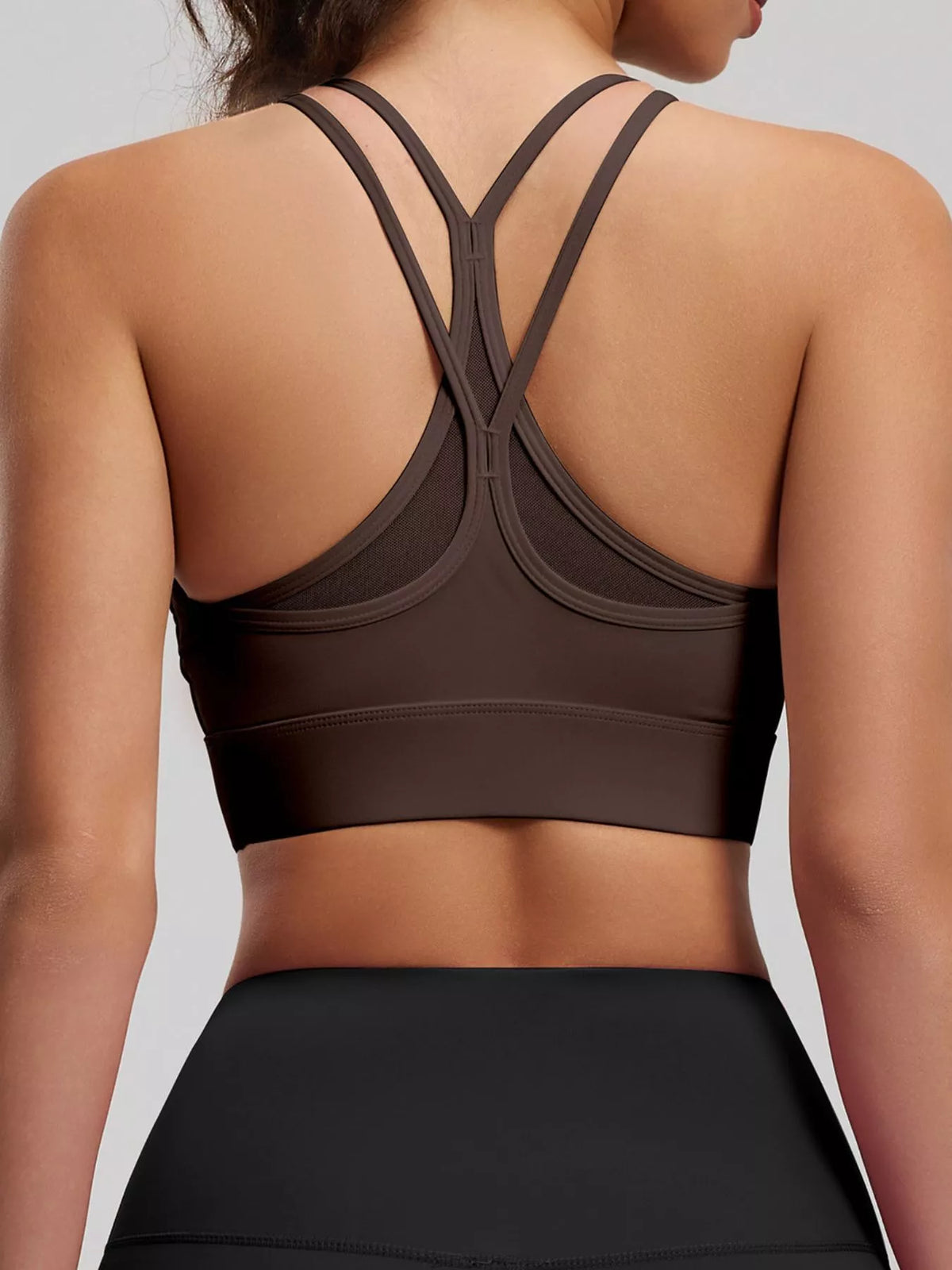 Back view of dark brown active bra showing crossed double straps above black leggings