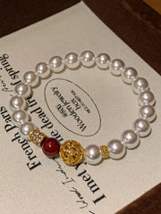Pearl bracelet with a gold filigree centerpiece and burgundy bead displayed on a printed card