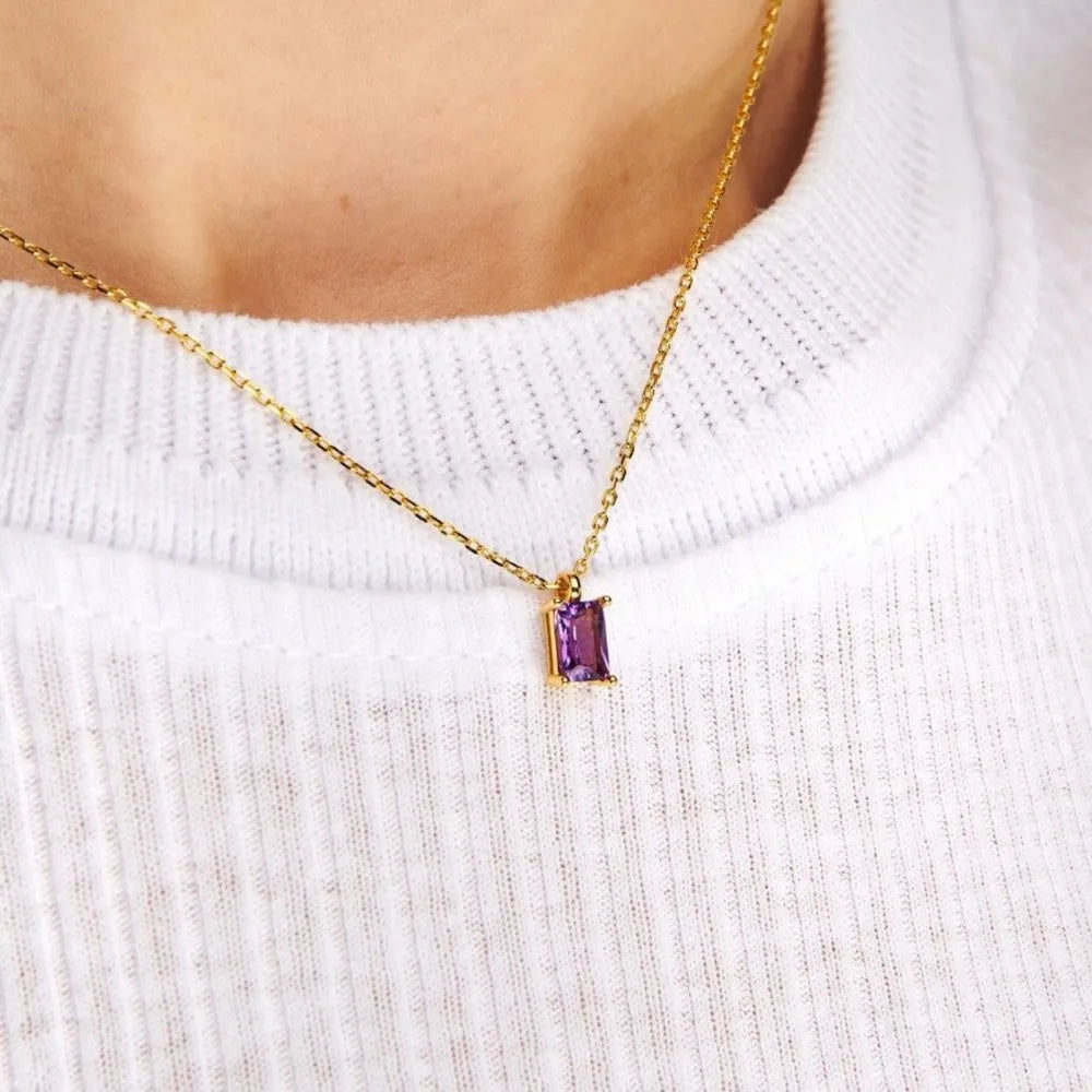 Purple rectangular pendant on a gold-tone chain worn over a white ribbed top