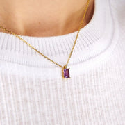 Purple rectangular pendant on a gold-tone chain worn over a white ribbed top