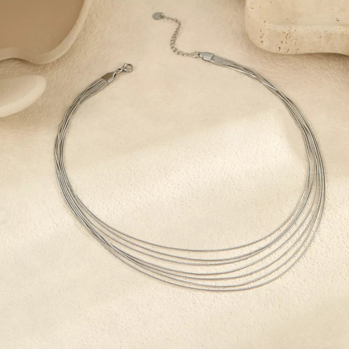 Close view of silver-tone layered necklace showing strands and clasp on cream surface