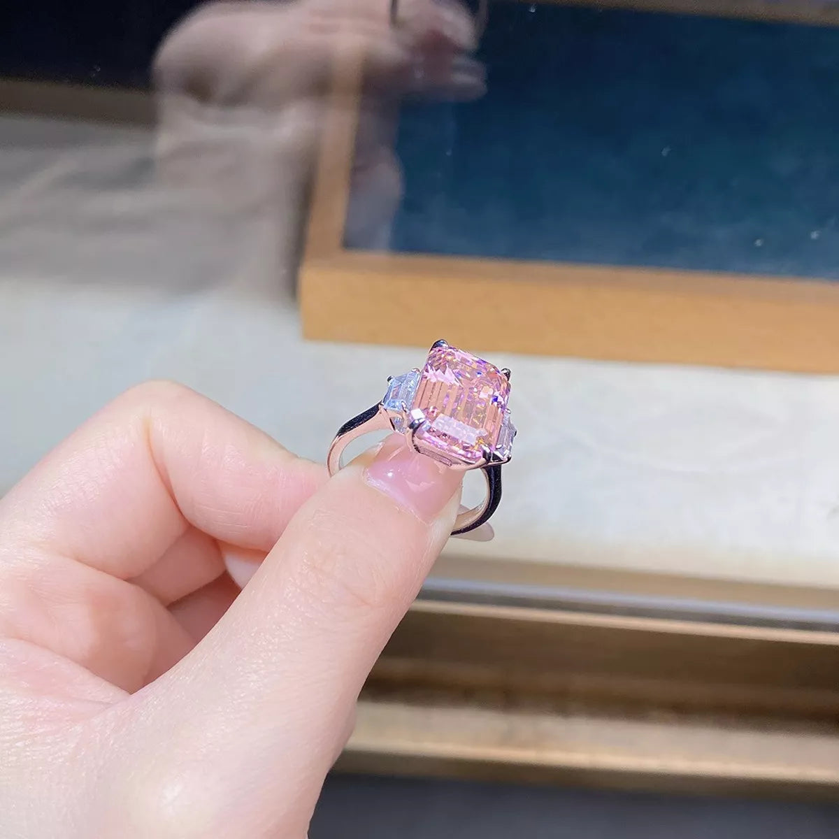 Close side view of the elevated rectangular pink center stone and clear side accents