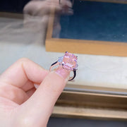 Close side view of the elevated rectangular pink center stone and clear side accents